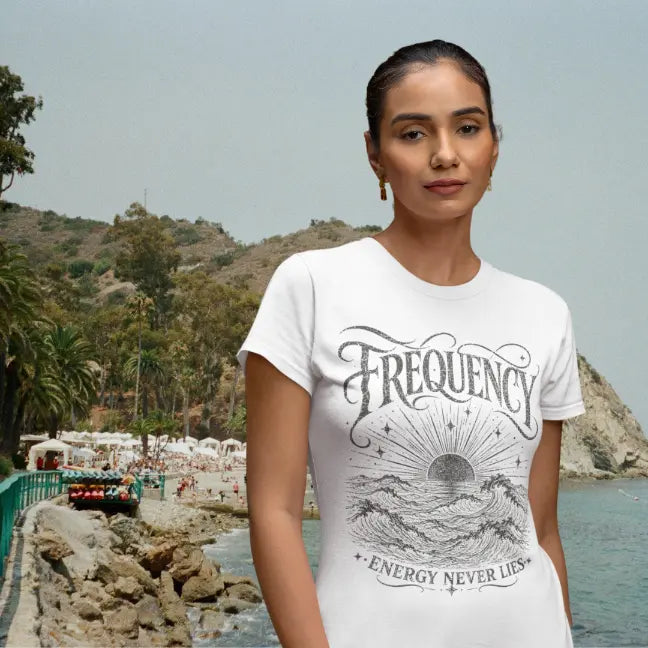 Model wearing white Frequency T-Shirt featuring distressed engraved sunrise and ocean wave design in relaxed coastal setting.