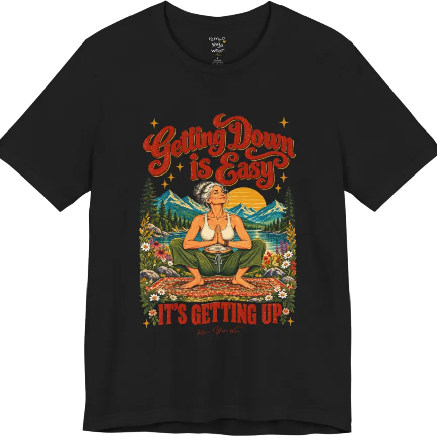 A short sleeved tee called the Getting Up T-Shirt, flat lay and a soft cotton blend shirt. Simply says, Getting Down is Easy, It's Getting Up. Design highlights retro red script lettering above a silver-haired person in a deep yoga squat with hands in prayer on a patterned mat, with a sun, mountains, a lake and wildflowers, bold red lettering for IT'S GETTING UP and a small script signature. Color is Black.