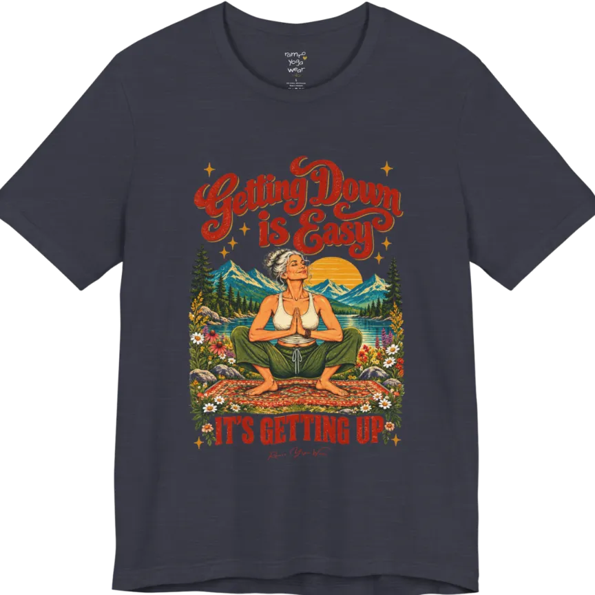 A short sleeved tee called the Getting Up T-Shirt, flat lay and a soft cotton blend shirt. Simply says, Getting Down is Easy, It's Getting Up. Design highlights retro red script lettering above a silver-haired person in a deep yoga squat with hands in prayer on a patterned mat, with a sun, mountains, a lake and wildflowers, bold red lettering for IT'S GETTING UP and a small script signature. Color is Heather Midnight Navy.