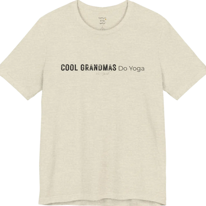 A short sleeved tee called the Grandmas T-Shirt, flat lay and a soft cotton blend shirt. Simply says, Cool Grandmas Do Yoga. Design highlights bold distressed block lettering for COOL GRANDMAS beside thin lettering for Do Yoga, with a small script signature underneath. Color is Heather Prism Natural.