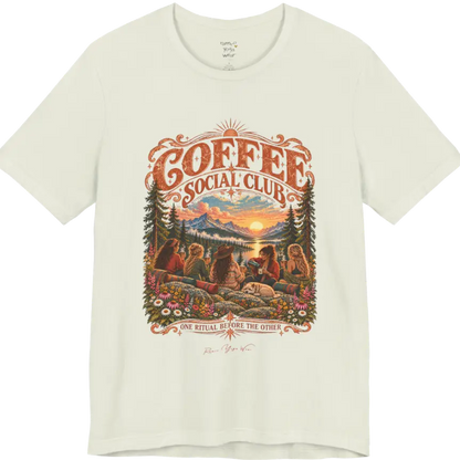 A short sleeved tee called the Grounds T-Shirt, flat lay and a Bella+Canvas 3001 shirt. Simply says, Coffee Social Club, One Ritual Before The Other. Design highlights a group of friends sharing coffee on a rocky mountain outcrop at sunrise, with rolled yoga mats, wildflowers, pine trees and a sleeping dog. Color is Citron.