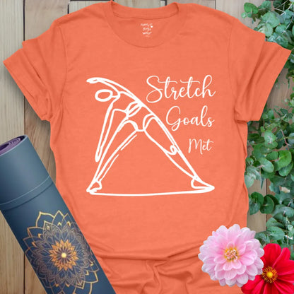 Vibrant orange t-shirt with dynamic stretch pose and playful “Stretch Goals Met” script for yoga practice and lifestyle wear.