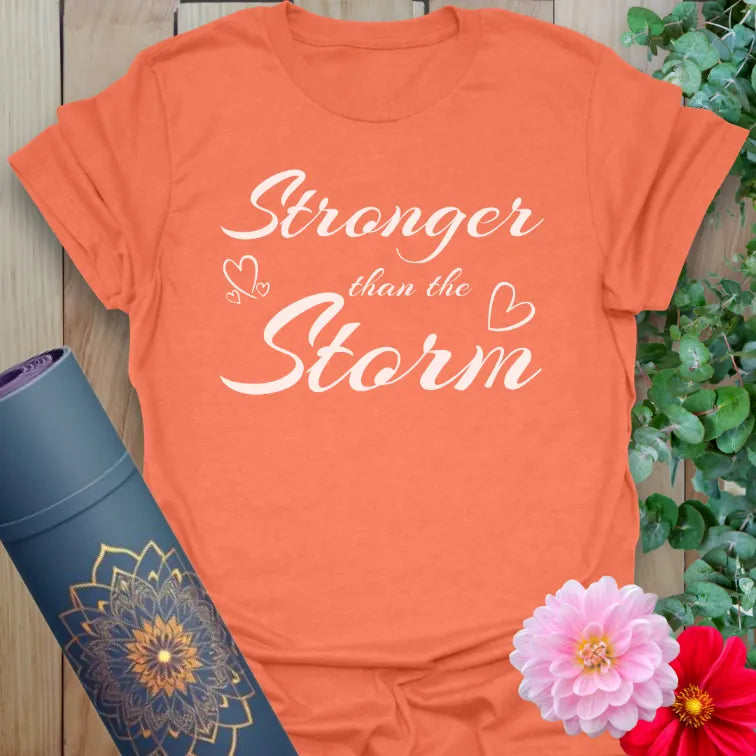 Vibrant orange tee with uplifting “Stronger than the Storm” phrase and gentle graphics for empowered mindfulness.