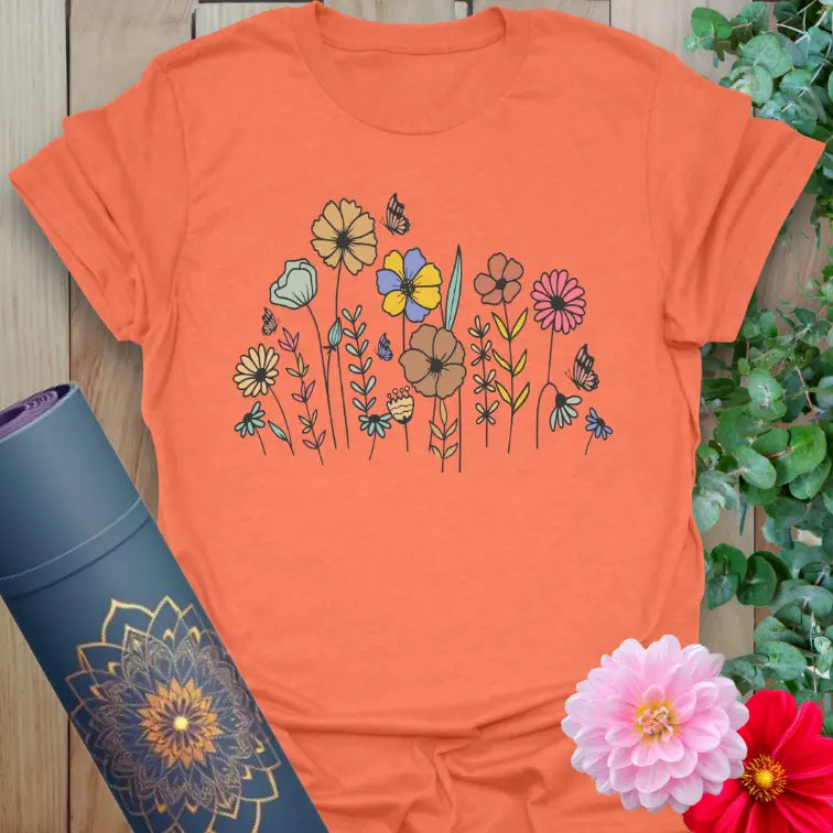 Vibrant orange t-shirt with colorful floral illustration and butterflies for joyful, nature-inspired movement.