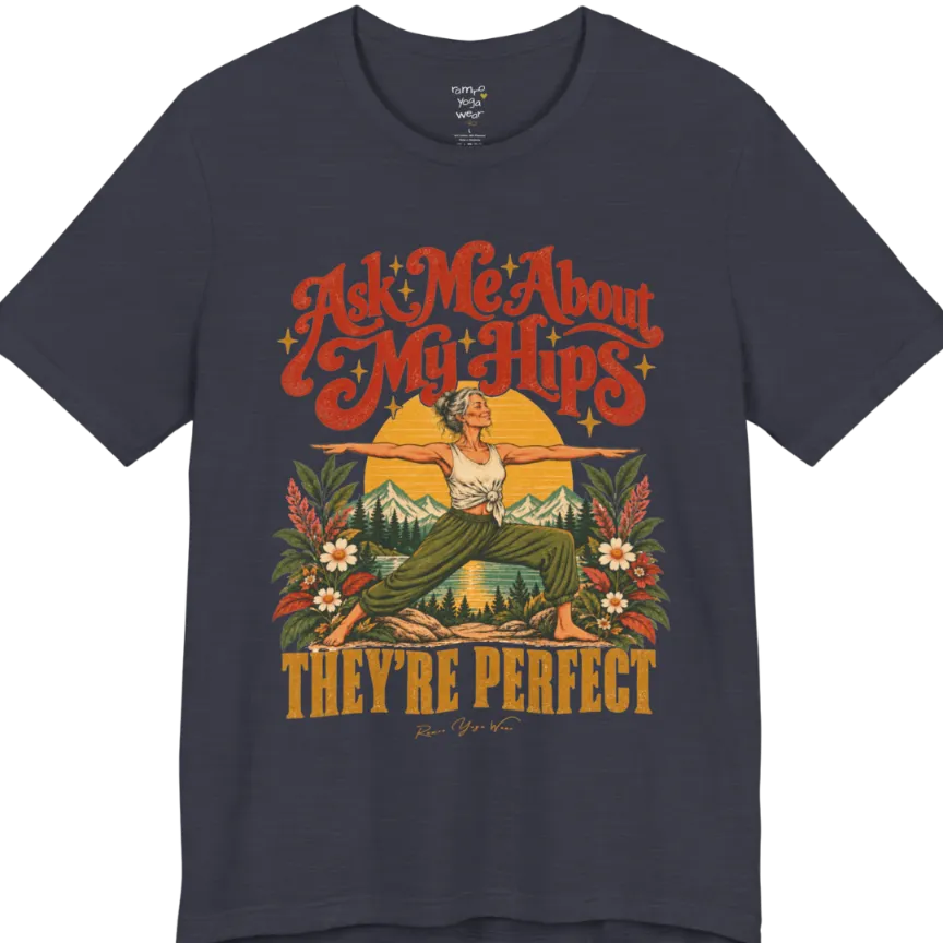 A short sleeved tee called the Hips T-Shirt, flat lay and a soft cotton shirt. Simply says, Ask Me About My Hips. They're Perfect. Design highlights a silver-haired woman in warrior two pose, arms outstretched and smiling, in front of a golden sun, mountains, a lake and wildflowers in a retro travel-poster style. Color is Heather Midnight Navy.