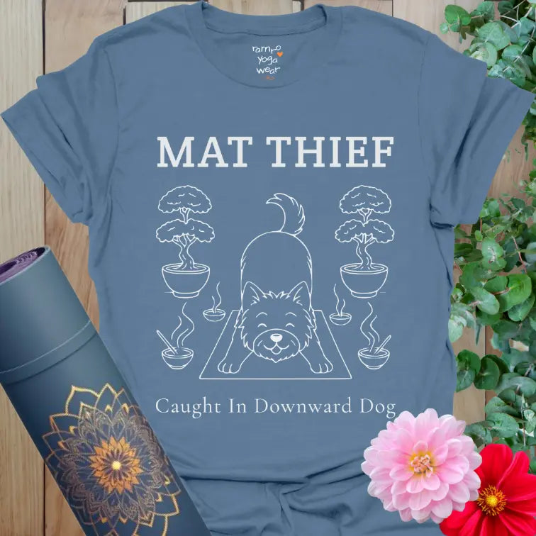Indigo Blue Mat Thief T-Shirt with a dog stretching on the mat among bonsai plants; playful yoga-dog design.