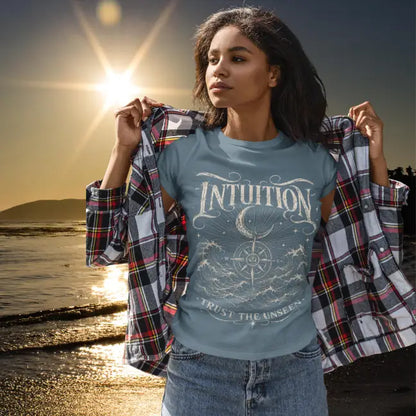 Woman wearing Stone Blue Intuition T-Shirt featuring engraved mystical ocean artwork with crescent moon and celestial detailing in warm golden coastal setting.