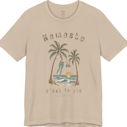 A short sleeved grunge tee with an illustrated scene of two palm trees framing a clothesline with leggings and a sports bra hanging between them, sun setting over waves, text reading "Namaste" and "c'est la vie" — Funny Yoga Shirts collection by Ramro Yoga Wear in Tan.