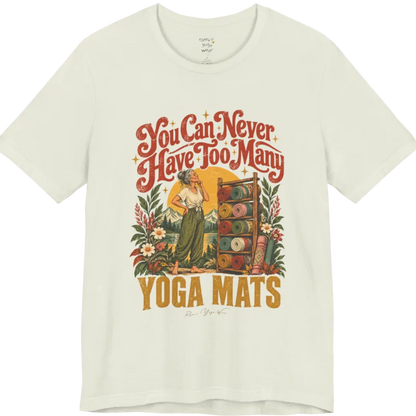 A short sleeved tee called the Mats T-Shirt, flat lay and a soft cotton shirt. Simply says, You Can Never Have Too Many Yoga Mats. Design highlights a silver-haired woman with her hand on her chin, deciding between a wooden rack of rolled yoga mats in rust, mustard, olive, teal and pink, in front of a golden sun, mountains and wildflowers in a retro travel-poster style. Color is Citron.
