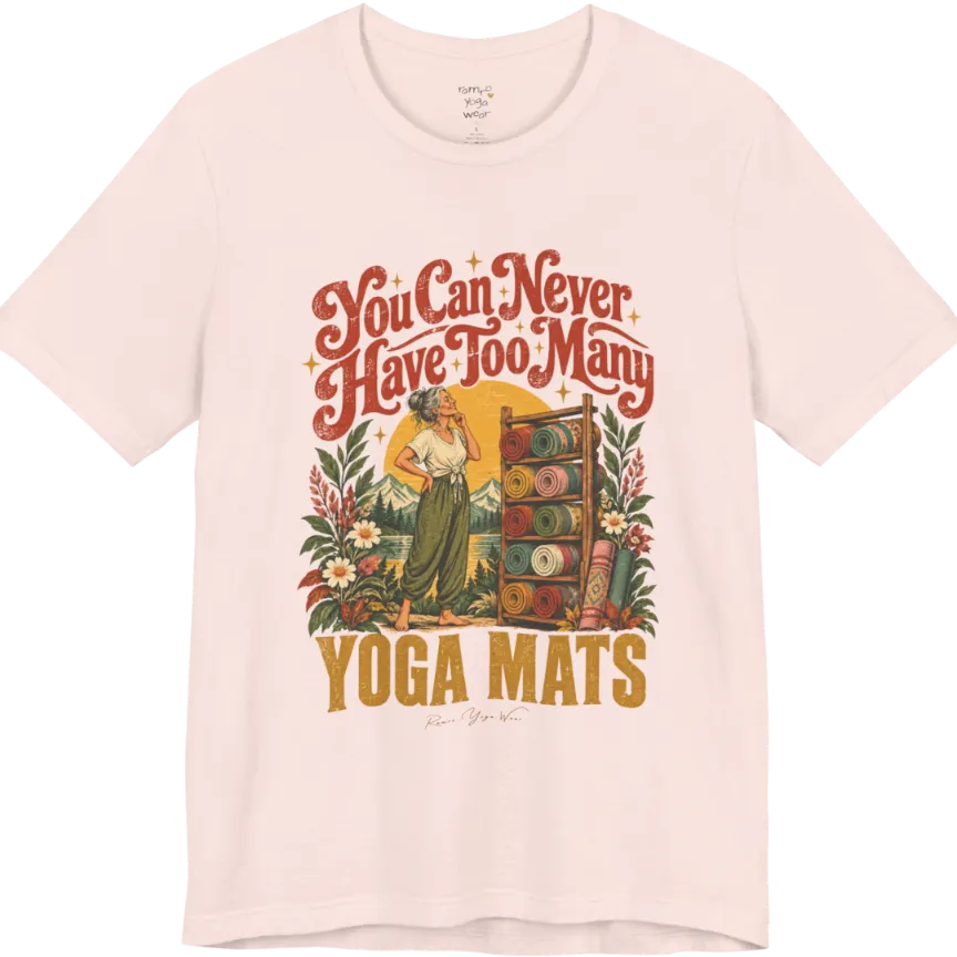 A short sleeved tee called the Mats T-Shirt, flat lay and a soft cotton shirt. Simply says, You Can Never Have Too Many Yoga Mats. Design highlights a silver-haired woman with her hand on her chin, deciding between a wooden rack of rolled yoga mats in rust, mustard, olive, teal and pink, in front of a golden sun, mountains and wildflowers in a retro travel-poster style. Color is Soft Pink.