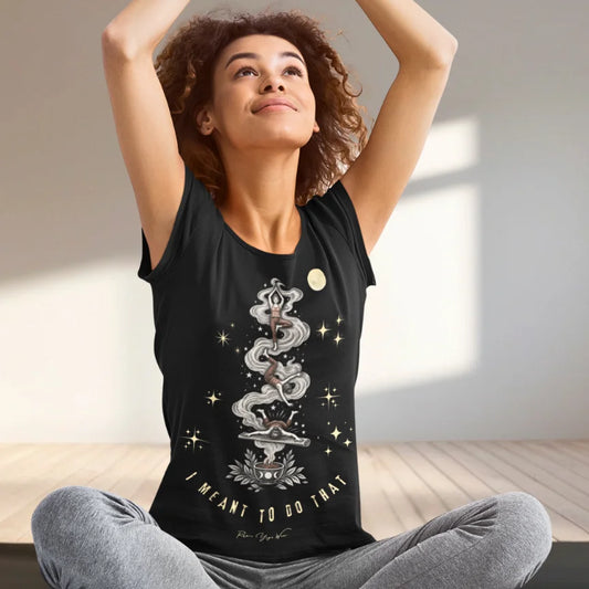 A woman sits cross-legged with her arms raised overhead on a wooden floor, wearing the Meant It T-Shirt. Meant It T-Shirt is a Bella+Canvas 3001 and the color is Black.