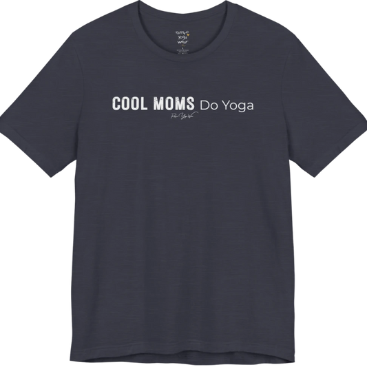 A short sleeved tee called the Moms T-Shirt, flat lay and a soft cotton shirt. Simply says, Cool Moms Do Yoga. Design highlights bold distressed block lettering for Cool Moms beside lighter thin lettering for Do Yoga, with a small script signature underneath. Color is Heather Midnight Navy.