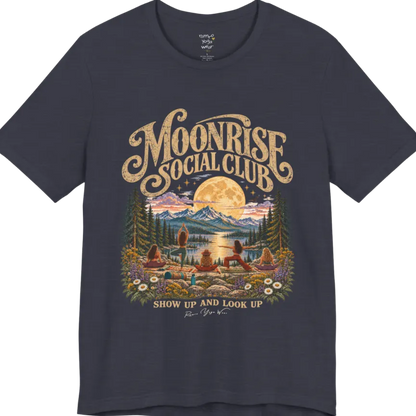 A short sleeved tee called the Moonrise T-Shirt, flat lay and a Bella+Canvas 3001. Simply says, Moonrise Social Club. Show Up And Look Up. Design highlights five women seen from behind practicing yoga on a rocky lakeside shelf, one in tree pose, one in warrior pose and three seated, beneath a glowing full moon rising over snow-capped mountains, framed by pine trees and wildflowers. Color is Heather Midnight Navy.