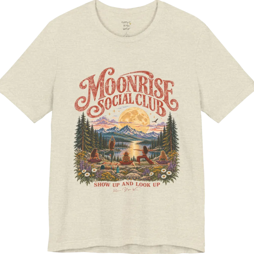 A short sleeved tee called the Moonrise T-Shirt, flat lay and a Bella+Canvas 3001. Simply says, Moonrise Social Club. Show Up And Look Up. Design highlights five women seen from behind practicing yoga on a rocky lakeside shelf, one in tree pose, one in warrior pose and three seated, beneath a glowing full moon rising over snow-capped mountains, framed by pine trees and wildflowers. Color is Heather Natural Prism. 
