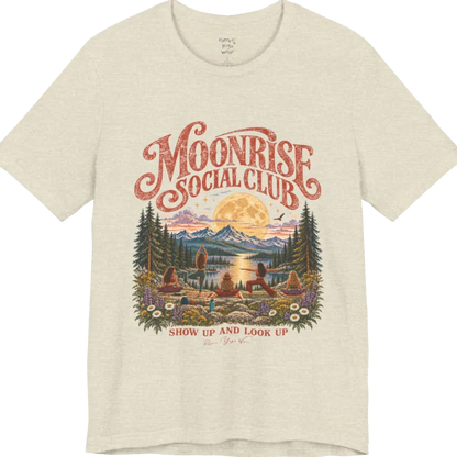 A short sleeved tee called the Moonrise T-Shirt, flat lay and a Bella+Canvas 3001. Simply says, Moonrise Social Club. Show Up And Look Up. Design highlights five women seen from behind practicing yoga on a rocky lakeside shelf, one in tree pose, one in warrior pose and three seated, beneath a glowing full moon rising over snow-capped mountains, framed by pine trees and wildflowers. Color is Heather Natural Prism. 