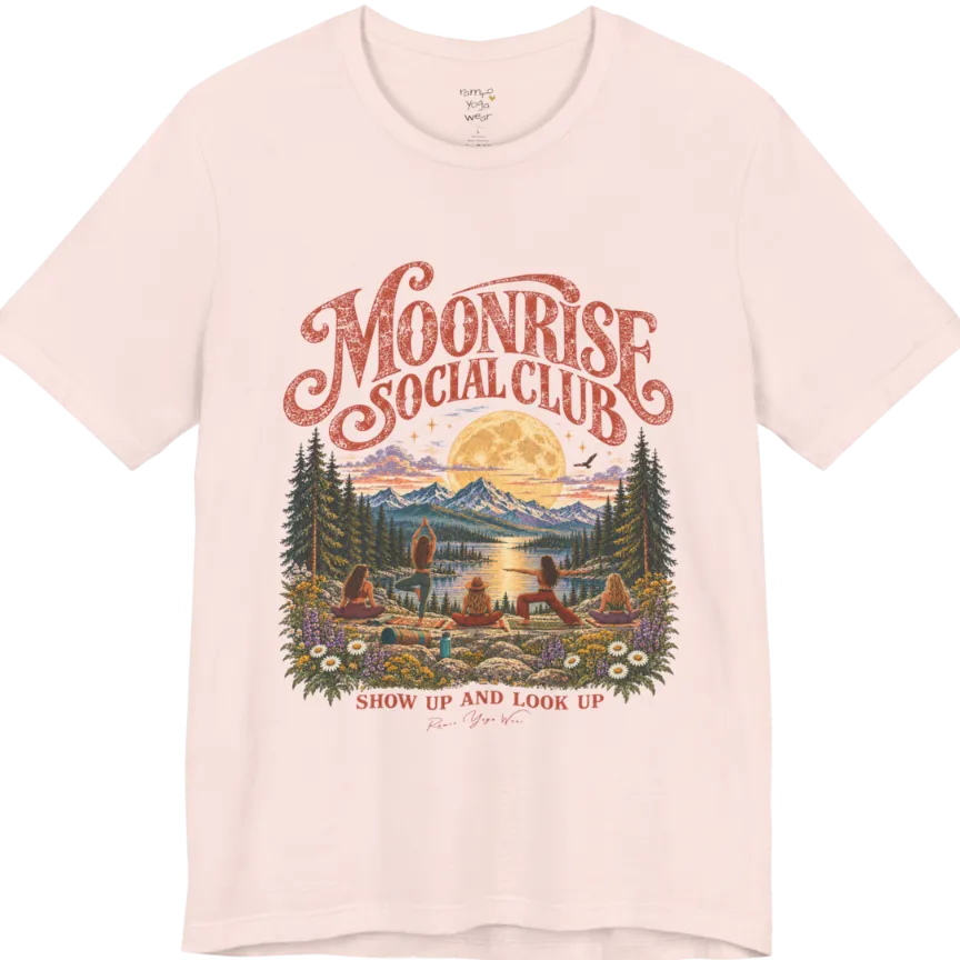 A short sleeved tee called the Moonrise T-Shirt, flat lay and a Bella+Canvas 3001. Simply says, Moonrise Social Club. Show Up And Look Up. Design highlights five women seen from behind practicing yoga on a rocky lakeside shelf, one in tree pose, one in warrior pose and three seated, beneath a glowing full moon rising over snow-capped mountains, framed by pine trees and wildflowers. Color is Soft Pink.