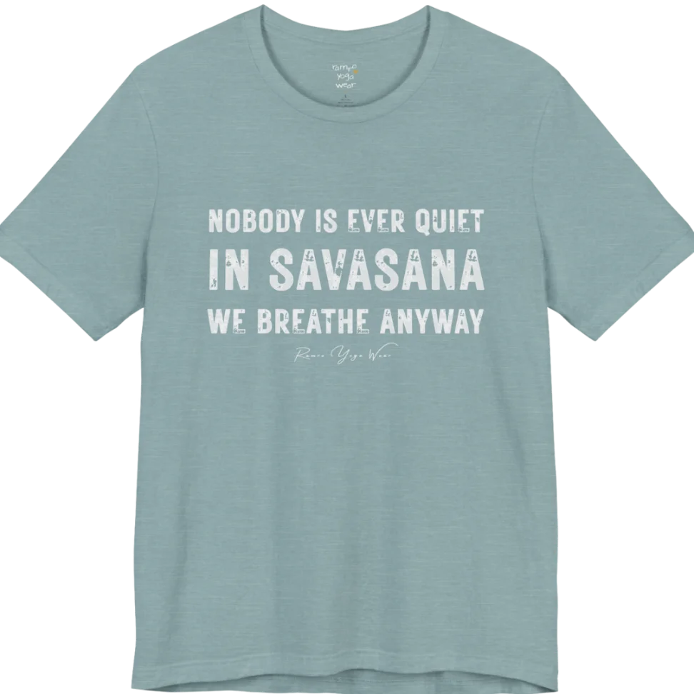 A short sleeved tee called the Nobody T-Shirt, flat lay and a soft cotton shirt. Simply says, Nobody is ever quiet in savasana. We breathe anyway. Design highlights three lines of bold condensed cream lettering with a small handwritten signature beneath. Color is Blue Lagoon.