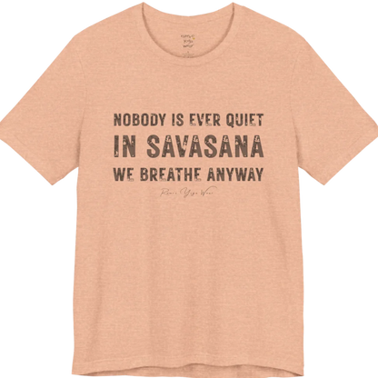 A short sleeved tee called the Nobody T-Shirt, flat lay and a soft cotton shirt. Simply says, Nobody is ever quiet in savasana. We breathe anyway. Design highlights three lines of bold condensed cream lettering with a small handwritten signature beneath. Color is Heather Peach.