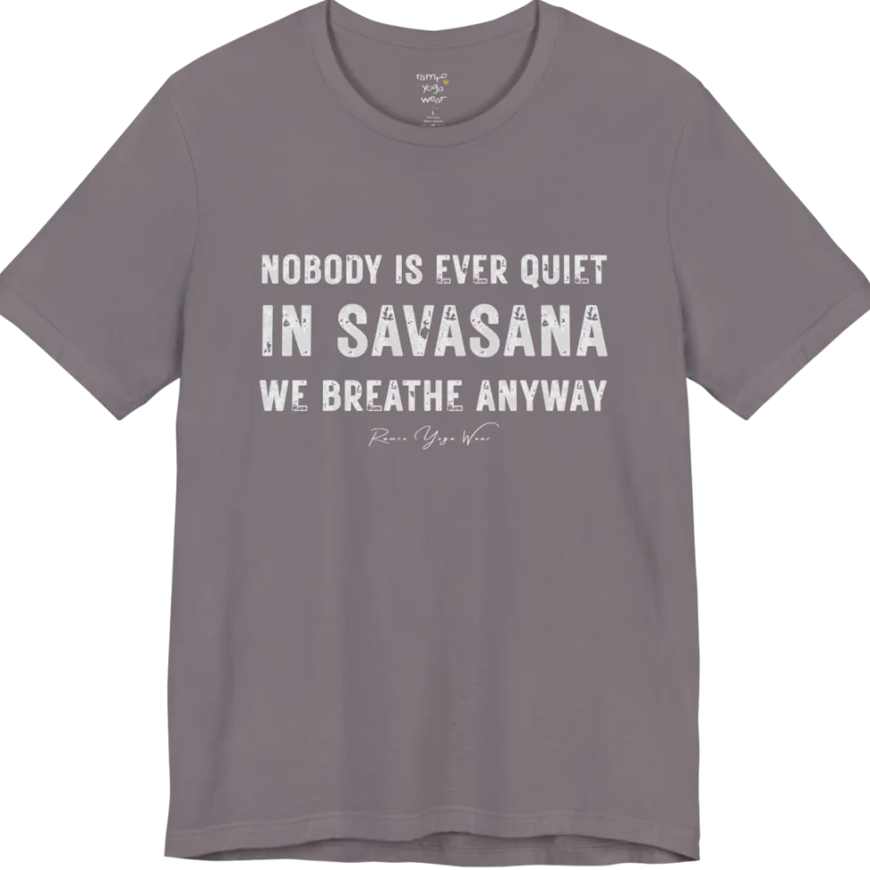 A short sleeved tee called the Nobody T-Shirt, flat lay and a soft cotton shirt. Simply says, Nobody is ever quiet in savasana. We breathe anyway. Design highlights three lines of bold condensed cream lettering with a small handwritten signature beneath. Color is Storm.