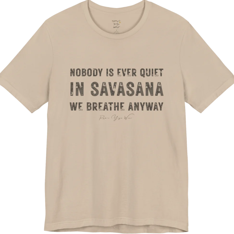 A short sleeved tee called the Nobody T-Shirt, flat lay and a soft cotton shirt. Simply says, Nobody is ever quiet in savasana. We breathe anyway. Design highlights three lines of bold condensed cream lettering with a small handwritten signature beneath. Color is Tan.