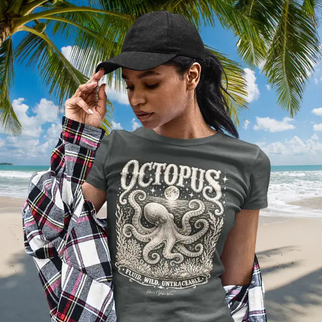 Woman wearing Octopus T-Shirt on the beach under palm trees, adjusting her cap, shirt in Dark Heather Grey