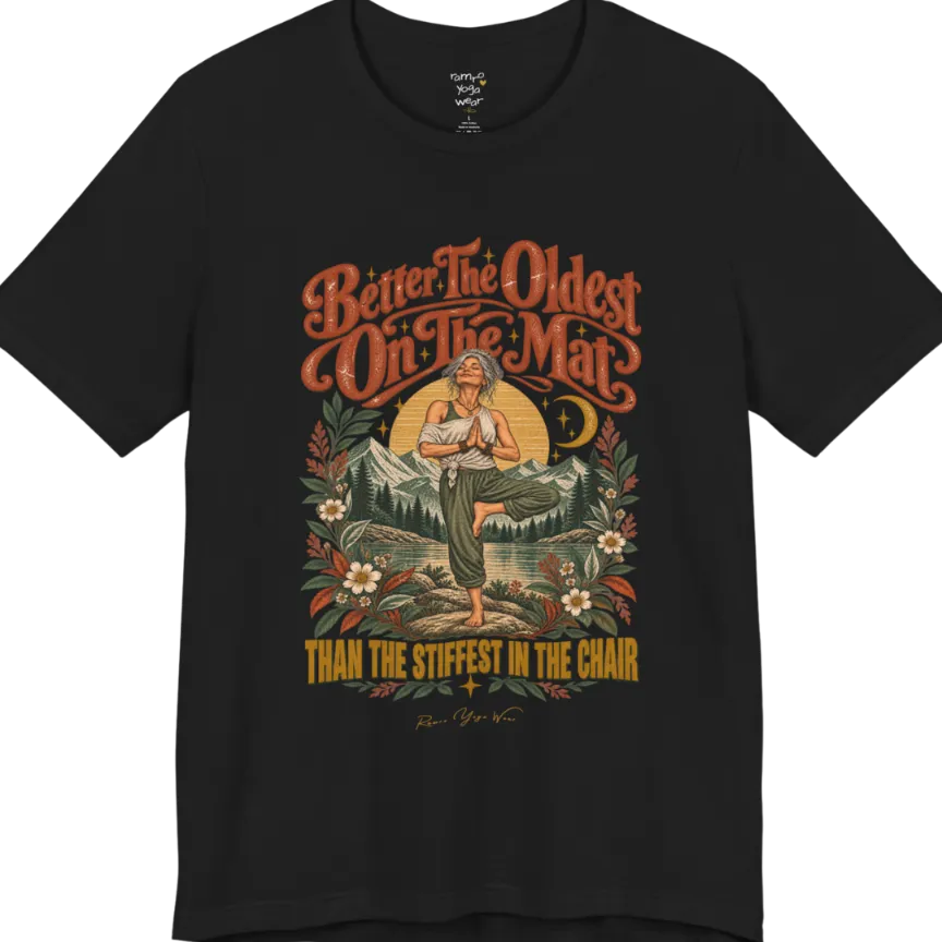 A short sleeved teed has an Illustration of an older woman in tree pose with hands in prayer position, standing on a rock by a lake, framed by mountains, pine trees, a sunburst, and botanical flowers. Oldest T-Shirt flat lay is a Bella+Canvas 3001 and the color is Black.