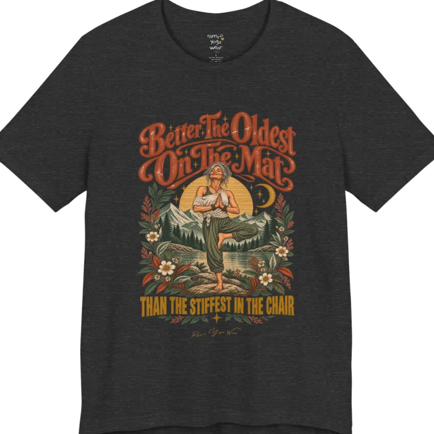 A short sleeved teed has an Illustration of an older woman in tree pose with hands in prayer position, standing on a rock by a lake, framed by mountains, pine trees, a sunburst, and botanical flowers. Oldest T-Shirt flat lay is a Bella+Canvas 3001 and the color is Dark Grey Heather.