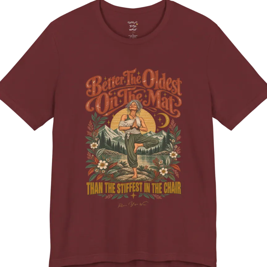 A short sleeved teed has an Illustration of an older woman in tree pose with hands in prayer position, standing on a rock by a lake, framed by mountains, pine trees, a sunburst, and botanical flowers. Oldest T-Shirt flat lay is a Bella+Canvas 3001 and the color is Heather Cardinal.