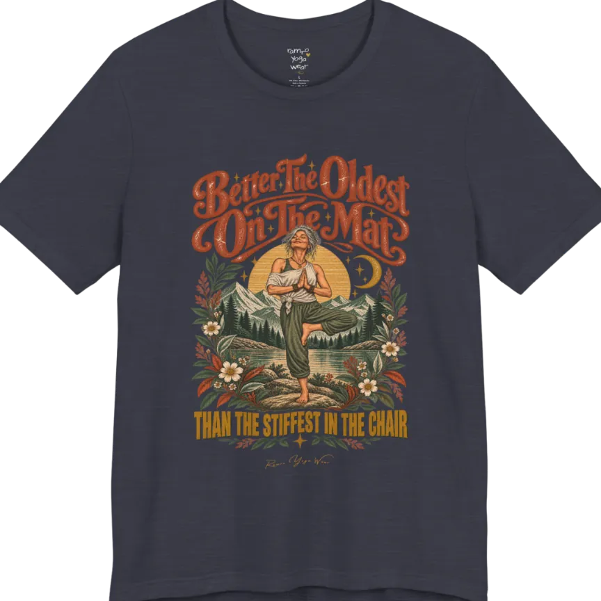 A short sleeved teed has an Illustration of an older woman in tree pose with hands in prayer position, standing on a rock by a lake, framed by mountains, pine trees, a sunburst, and botanical flowers. Oldest T-Shirt flat lay is a Bella+Canvas 3001 and the color is Heather Midnight Navy.