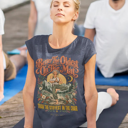 A woman is in Cobra Pose with her eyes closed at her yoga class, other participants around her, wearing the Oldest T-Shirt. Oldest T-Shirt is a Bella+Canvas 3001 and the color is Heather Midnight Navy.