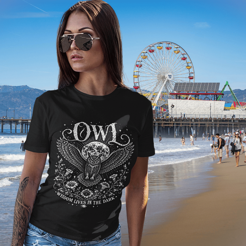 Lifestyle image of woman wearing the Owl T-Shirt at the beach with vintage owl illustration, celestial moon graphic, and mystical aesthetic.