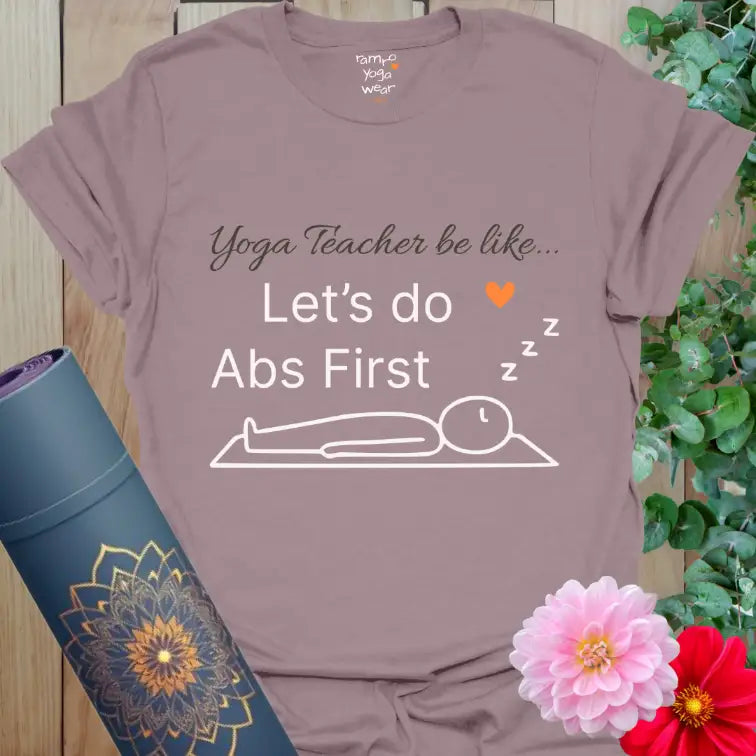 Paragon Abs First T-Shirt with playful yoga quote “Yoga Teacher be like… Let’s do Abs First” and minimalist line-art figure in Savasana.