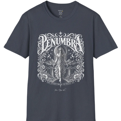 A short sleeved tee called the Penumbra T-Shirt, flat lay and a Gildan 64000 shirt. Simply says, Not Everything Is Fully Lit. Design highlights a moon goddess bathed in radiant light against a mountain backdrop, framed in ornate vintage lettering with botanical detailing. Color is Heather Navy.