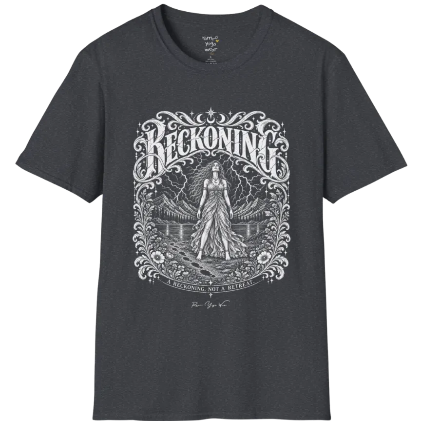 A short sleeved tee called the Reckoning T-Shirt, flat lay and a soft cotton shirt. Simply says, A reckoning, not a retreat. Design highlights ornate white RECKONING lettering framed by flourishes and wild florals, with a long-haired figure in a flowing gown walking a footprint path toward a lightning storm over mountains and a lake. Color is Dark Heather Grey.