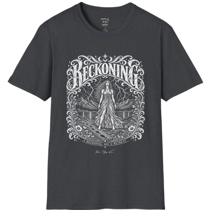 A short sleeved tee called the Reckoning T-Shirt, flat lay and a soft cotton shirt. Simply says, A reckoning, not a retreat. Design highlights ornate white RECKONING lettering framed by flourishes and wild florals, with a long-haired figure in a flowing gown walking a footprint path toward a lightning storm over mountains and a lake. Color is Dark Heather Grey.