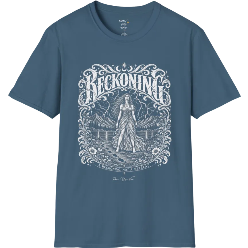 A short sleeved tee called the Reckoning T-Shirt, flat lay and a soft cotton shirt. Simply says, A reckoning, not a retreat. Design highlights ornate white RECKONING lettering framed by flourishes and wild florals, with a long-haired figure in a flowing gown walking a footprint path toward a lightning storm over mountains and a lake. Color is Indigo Blue.