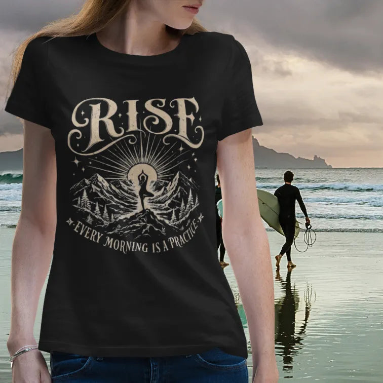 Woman wearing Black Rise T-Shirt by the ocean with vintage yoga graphic and calm grounded lifestyle styling.