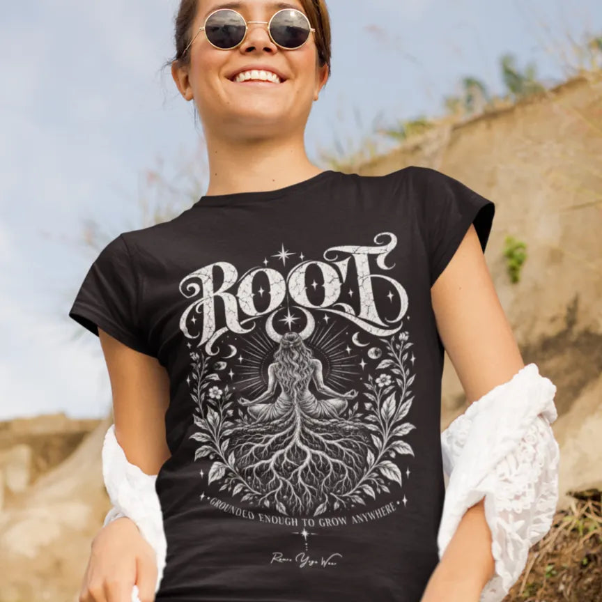 A woman smiles in sunglasses against a stone wall backdrop, wearing the Root T-Shirt. Root T-Shirt is a Gildan 64000 and the color is Black.