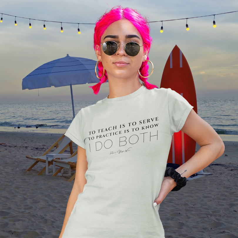 Woman wearing Sacred Work Citron yoga teacher gift tee on the beach near a surfboard — Yoga Teacher Gifts collection by Ramro Yoga Wear