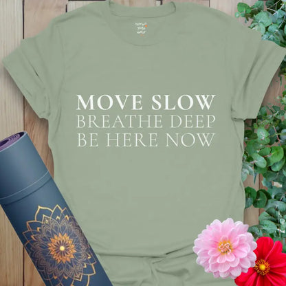 Sage Be Here Now T-Shirt with white serif lettering reading “Move Slow • Breathe Deep • Be Here Now.” Calm, earthy yoga top for everyday mindfulness.