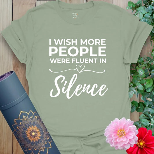 Calm sage green yoga t-shirt featuring "Fluent in Silence" quote and heart design promoting conscious stillness and mindful self-expression.