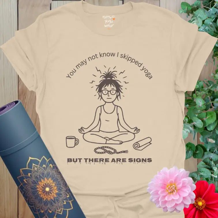 Sand Signs T-Shirt with black line-art yogi design and text “You may not know I skipped yoga, but there are signs.” Soft earthy yoga humor tee.