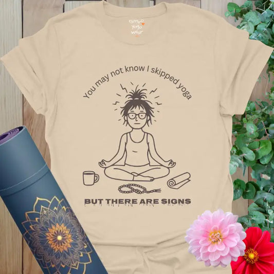 Sand Signs T-Shirt with black line-art yogi design and text “You may not know I skipped yoga, but there are signs.” Soft earthy yoga humor tee.