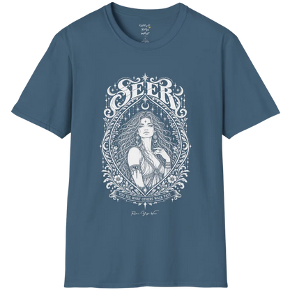 A short sleeved tee called the Seer T-Shirt, flat lay and a soft cotton shirt. Simply says, You see what others walk past. Design highlights an ornate engraved almond-shaped frame of florals and filigree around a close portrait of a long-haired figure with a star on the brow, crescent moon earrings and one hand at the collarbone, beneath a crescent moon and hanging stars, with Seer in decorative lettering across the top and the tagline on a banner below. Color is Indigo Blue.