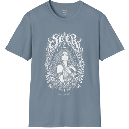 A short sleeved tee called the Seer T-Shirt, flat lay and a soft cotton shirt. Simply says, You see what others walk past. Design highlights an ornate engraved almond-shaped frame of florals and filigree around a close portrait of a long-haired figure with a star on the brow, crescent moon earrings and one hand at the collarbone, beneath a crescent moon and hanging stars, with Seer in decorative lettering across the top and the tagline on a banner below. Color is Stone Blue.
