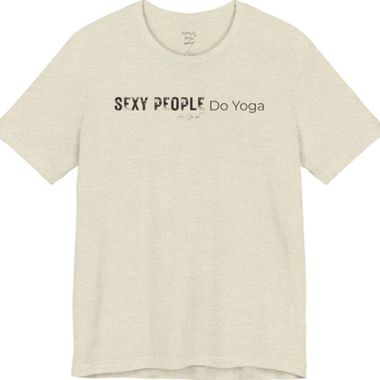 A short sleeved tee called the Sexy T-Shirt, flat lay and a soft cotton shirt. Simply says, Sexy People Do Yoga. Design highlights bold distressed block lettering for Sexy People beside lighter thin lettering for Do Yoga, with a small script signature underneath. Color is Heather Prism Natural.