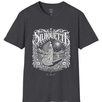 A short sleeved tee called the Silhouette T-Shirt, flat lay and a Gildan 64000 shirt on a white background. Simply says, Light Doesn't Lie About Your Shape. Design highlights a long-haired figure in a flowing gown gazing at a radiating star, framed by ornate florals, mountains and a lake, with the figure's cast shadow on the path. Color is Dark Heather Grey.