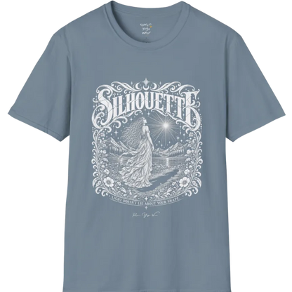 A short sleeved tee called the Silhouette T-Shirt, flat lay and a Gildan 64000 shirt on a white background. Simply says, Light Doesn't Lie About Your Shape. Design highlights a long-haired figure in a flowing gown gazing at a radiating star, framed by ornate florals, mountains and a lake, with the figure's cast shadow on the path. Color is Stone Blue.