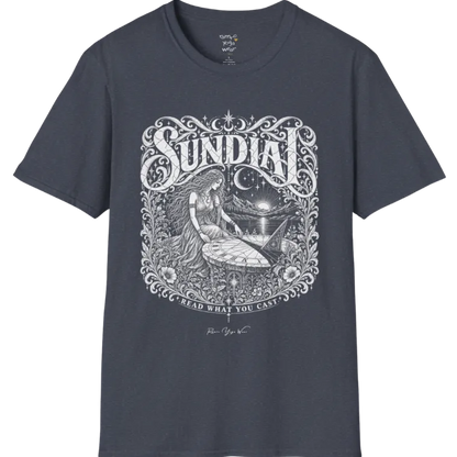 A short sleeved tee called the Sundial T-Shirt, flat lay and a Gildan 64000 shirt. Simply says, Read What You Cast. Design highlights a woman reading a sundial beneath a starry sky, with mountains and a rising sun in the background, in a detailed vintage-inspired illustration. Color is Heather Navy.