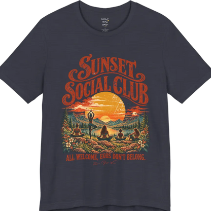 A short sleeved tee called the Sunset T-Shirt, flat lay and a Bella + Canvas 3001 shirt. Simply says, Sunset Social Club, All Welcome, Egos Don't Belong. Design highlights several people meditating together across a mountain landscape at sunset, with a large setting sun, pine trees, and florals, in a color vintage travel-poster illustration. Color is Heather Midnight Navy.